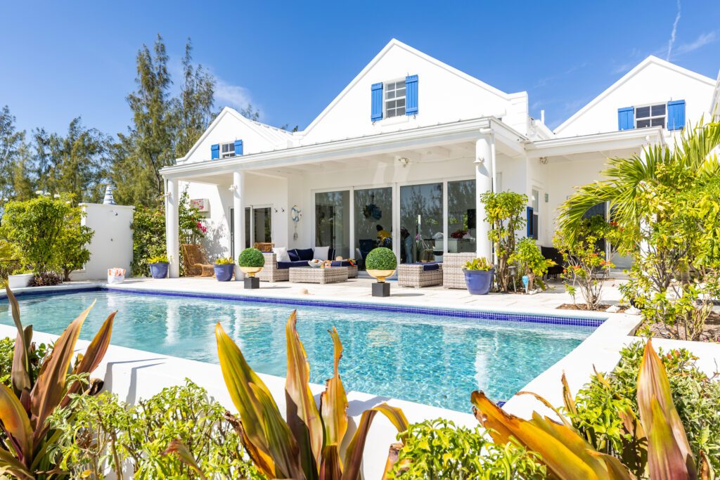 Luxury white villa with a swimming pool, surrounded by lush greenery under a clear blue sky.