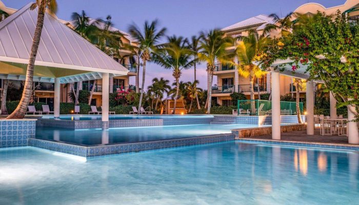 Tropical resort pool at sunset with palm trees.