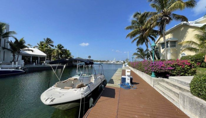 Boat docked near waterfront houses and palm trees.