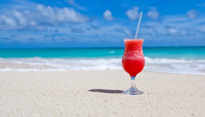 Red drink on sandy beach, ocean background.